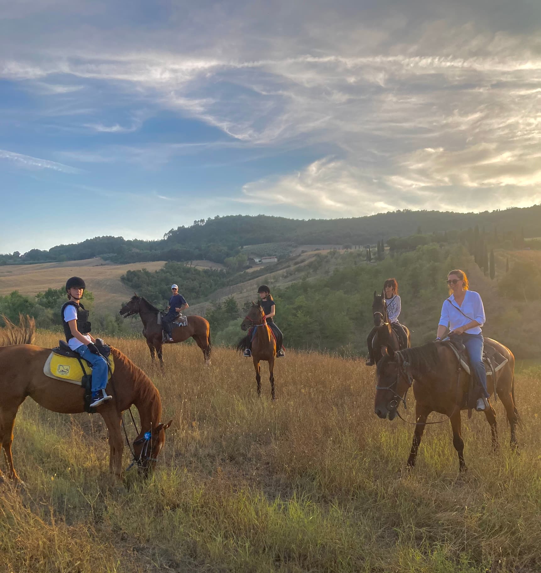 A group riding horses through the Tuscan countryside at sunset